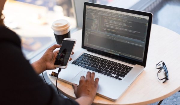Man charging phone whilst coding on laptop